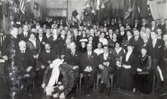 1916 Uitreiking der prijzen 1e Rondvaart door Nederland, in het American-Hotel
Zaterdag 30 October 1915 heeft in American-Hotel te Amsterdam de feestelijke prijs-uitdeeling plaats gevonden van den zoo welgeslaagden Vijf-Provinciën-Toer, welke van 15 Juni tot 15 September 1915 door het Comité voor Wherry-wedstrijden te Amsterdam werd georganiseerd. Reeds meermalen werd in dit tijdschrift van het groote nut, van de uitnemende propaganda gewaagd, welke dit evenement voor het water-tourisme, voor de watersport in het algemeen, heeft gehad. En Zaterdag werd de kroon op het werk gezet. De feestzaal van American-Hotel was, mede door de welwillendheid van „Het Jagershuis" te Amsterdam, welke inrichting tal van wimpels en vanen beschikbaar stelde, keurig en kleurig versierd, terwijl tevens aan de wanden tal van geïllustreerde artikelen uit verschillende bladen, den Toer betreffende, en soortgelijke foto's waren aangebracht. Het een en ander was te danken aan den ceremoniemeester van den avond,, van den ganschen toer, den ijverigen secretaris, den heer C. H. M. Philippona. Jhr. W. Six, de voorzitter der „Koninklijke", sprak de feestrede uit, en overhandigde verder de artistiek uitgevoerde diploma's aan hen, dié den Toer volbrachten. En dat waren er velen, zoodat het gezellig was en vol in American, een stemming, nog verhoogd door haitelijke bijvalsuitingen en clubliederen der vereenigingen, door pittig strijkje gespeeld. Behalve Jhr. Six voerden nog de HH. Muysken en Kok het woord. De laatste bracht, in zijne hoedanigheid van voorzitter van Willem III, den heer Philippona warme hulde voor het initiatief en de correcte uitvoering daarvan, en overhandigde den secretaris onder applaus en hoera-geroep êen lauwerkrans. Bovenstaande foto zij een herinnering aan den schoonen avond! Op den voorgrond ziet men v.l.n.r. de HH. J. H. Glasbergen, Jhr. W. Six, C. H. M. Philippona, C. H. S. Brons (achter den heer Philippona staande), F. C. Muysken