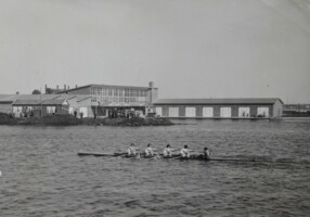 1954 Dameshead. Johanna Jacoba de Ruijter (boeg), Elly Jacoba Johanna van de Haas, Wilhelmina Frederika Baaren, Petronella Groenewegen van Wijk (slag), Barbara Jullien (stv) (zie Bluflijst in DL1954_11). Het nog niet geopende Clubhuis op de achtergrond, met bouwloods en zonder vlaggenmast.